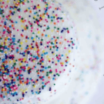 Close-up of a white frosted cake topped with colorful sprinkles, made even more delectable with a smooth layer of pourable faux fondant icing. The background is blurred, focusing attention on the cake's stunning decoration.