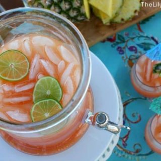A pitcher of rum punch with limes and pineapples.