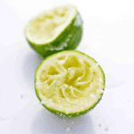Two halves of a squeezed lime are shown on a white surface, with some lime pulp and juice visible, perfect for your Salted Lime Tequila Shooters.