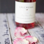 Candied rose petals delicately arranged next to a bottle of wine on a wooden table.