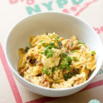 A white bowl filled with pizza eggs, garnished with chopped chives, placed on a cardboard surface.