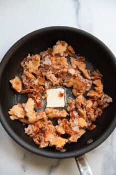 Cooked ground meat with a pat of butter is heating in a black skillet on a marble countertop, ready to be transformed into savory Pizza Eggs.