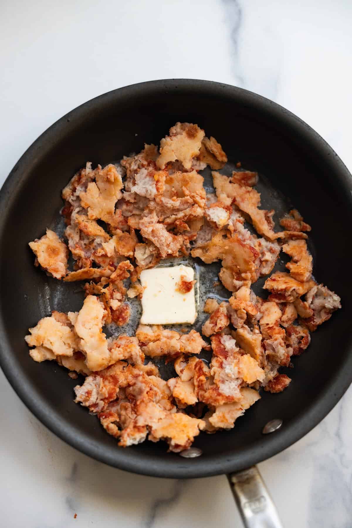 Cooked ground meat with a pat of butter is heating in a black skillet on a marble countertop, ready to be transformed into savory Pizza Eggs.