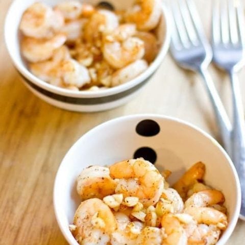 Two bowls of salt and pepper shrimp on a wooden table.