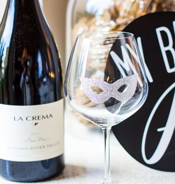 A festive wine glass decked out with Halloween decals sits alongside a bottle of wine.