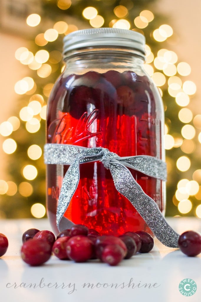 mason jar full of cranberry moonshine with cranberries in it. Lights in the background. 