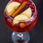 A glass of cranberry apple punch with cinnamon sticks and apples.