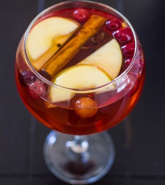 A glass of cranberry apple punch with cinnamon sticks and apples.