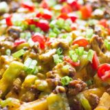 A close up of French Fry Nachos topped with meat and vegetables.