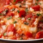 Close-up of easy Tuscan baked fish fillet topped with diced tomatoes, onions, capers, and chopped herbs in a savory tomato-based sauce.