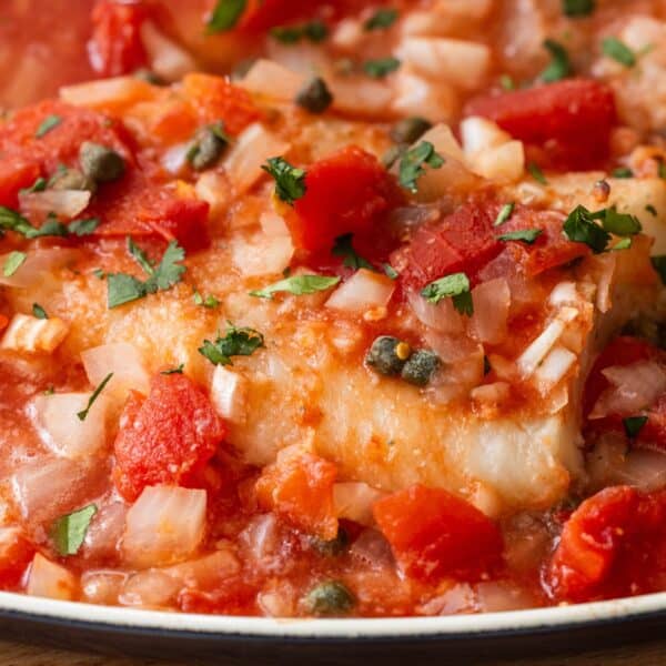 Close-up of easy Tuscan baked fish fillet topped with diced tomatoes, onions, capers, and chopped herbs in a savory tomato-based sauce.