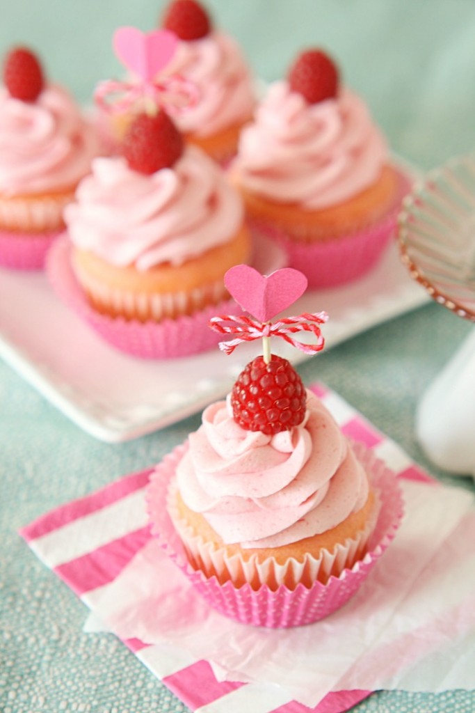 pink cupcake with pink icing and a raspberry on top some in the background