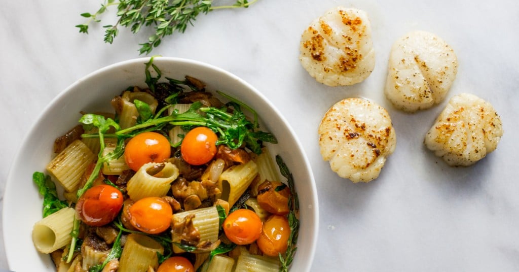 pasta, arugula, tomatoes, mushrooms with four scallops in the background