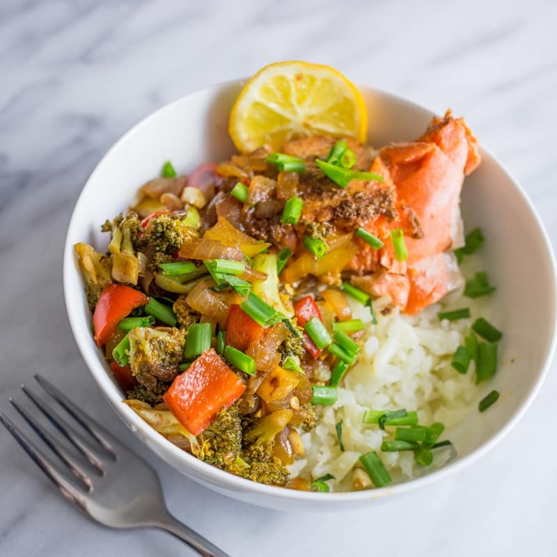 bowl with rice, salmon, broccoli, chives, and lemon in it