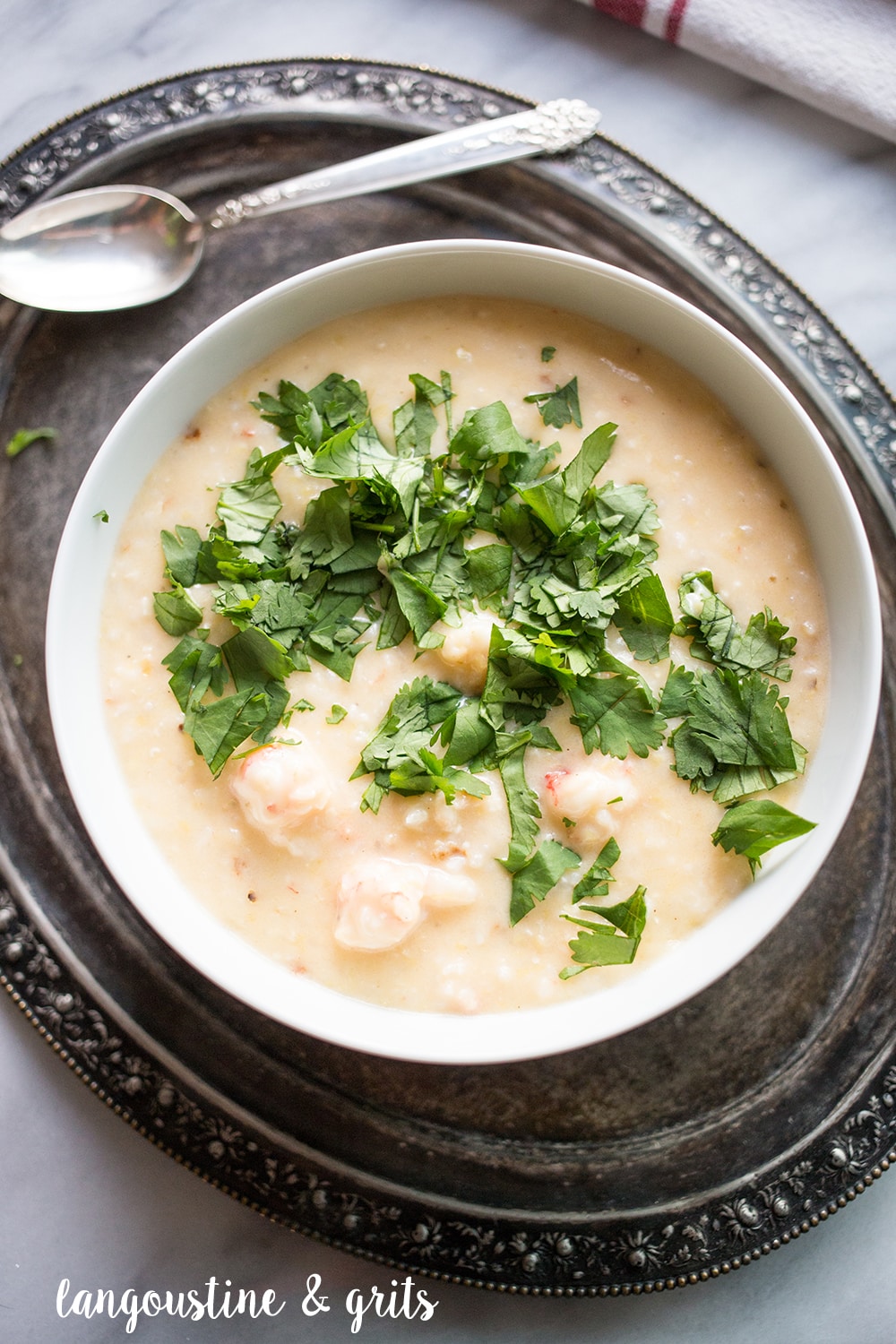 creamy grits with chunks of langoustine in a white bowl topped with parsley
