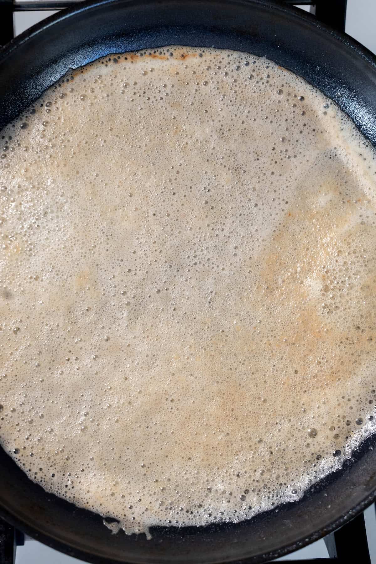 A thin crepe is cooking in a black frying pan on a stovetop, perfect for making sweet treats—or even as a savory base for perfect pan seared scallops.