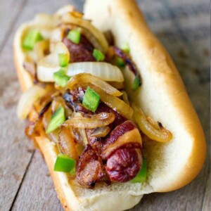 bacon wrapped hot dog on a bun with onions and jalapenos on it
