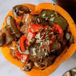 Spicy vegan stuffed bell pepper with diced tomatoes, mushrooms, and herbs on top, served on a white plate.