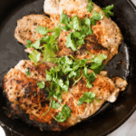 Grecian flavors come alive with grilled chicken breasts, delicately garnished with fresh cilantro in a black skillet.