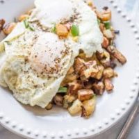 Cheesy veggie homefries with fried eggs on a skillet.