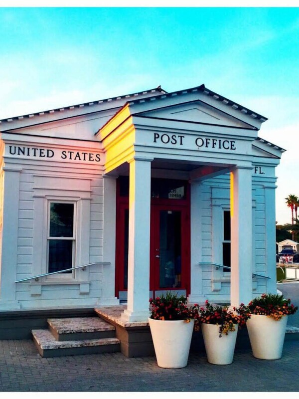 A white post office building with potted plants in front of it, symbolizing 6 months post-surgery recovery.
