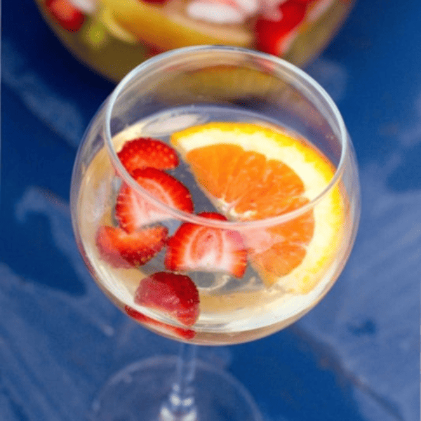 A glass of the best white sangria garnished with sliced strawberries and an orange wedge.