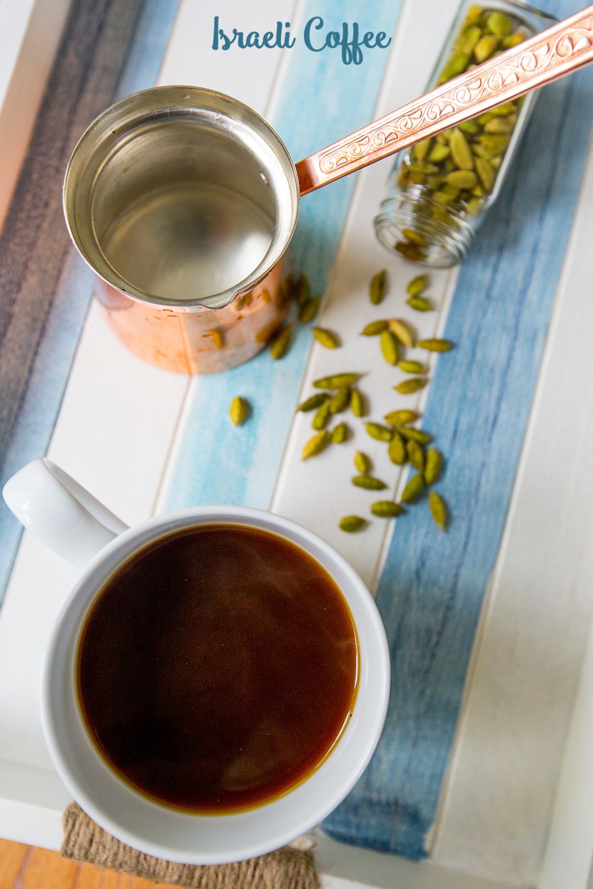 espresso pot and cardamom pods on a table with white mug of coffee