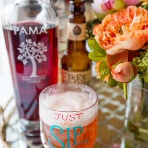 A glass of wine and a pomegranate beer-ita on a table.