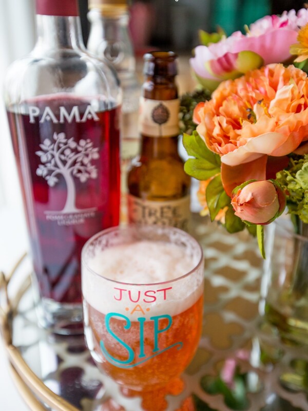 A glass of wine and a pomegranate beer-ita on a table.