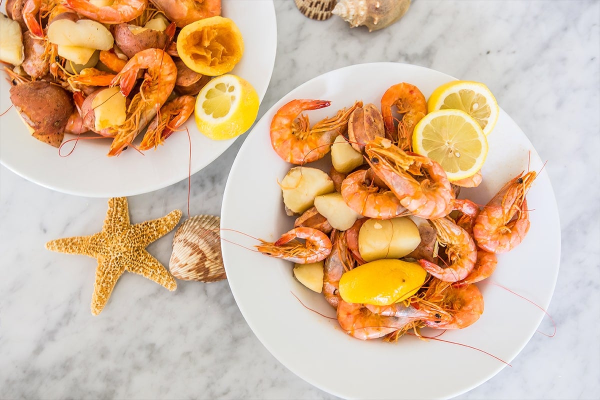 white plates with shrimp, potatoes, and lemon on them