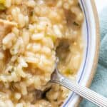 A close-up of a bowl of creamy risotto with pieces of chicken and herbs, being scooped with a fork. This easy chicken risotto recipe is perfect for one-pot cooking.