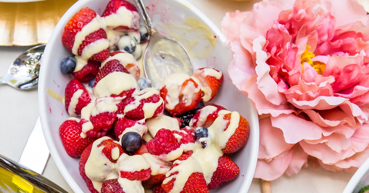 strawberries, blueberries, and raspberries in a bowl with cream and a spoon