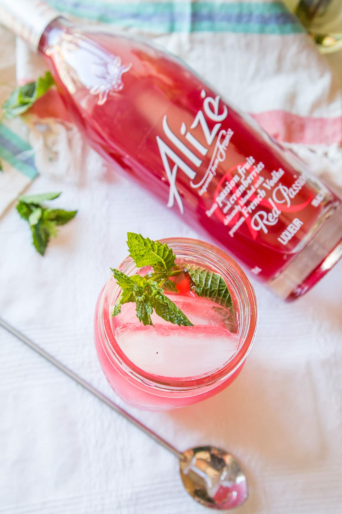 jar with pink cocktail, lemon, and mint in it with Alize in the background