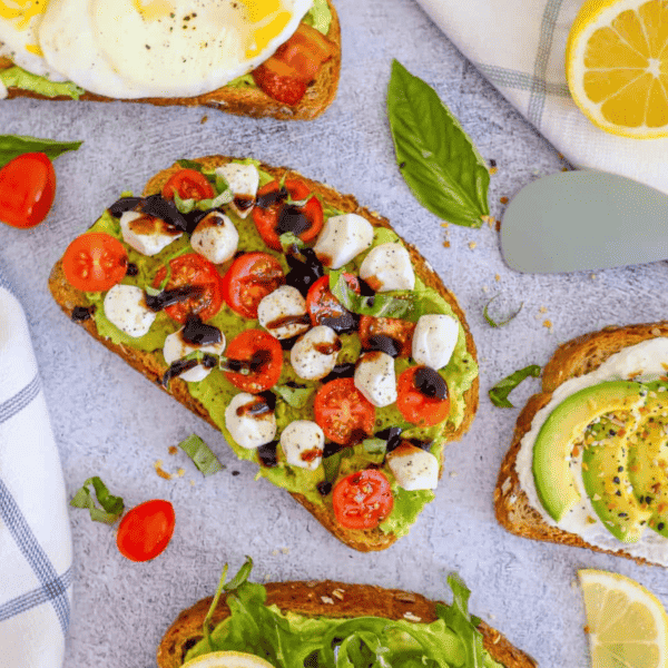 Four slices of avocado toasts with tomatoes and lemons.