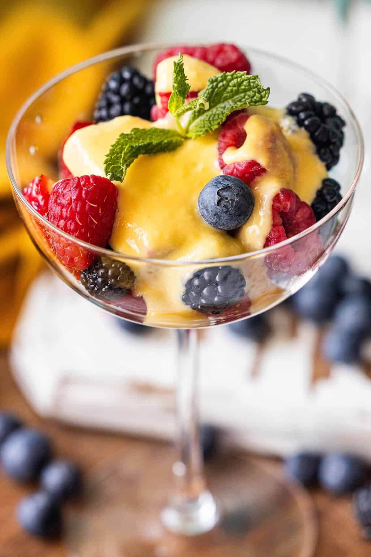 A glass filled with fresh raspberries, blackberries, and blueberries, topped with a silky creme anglaise and garnished with mint—a delightful berries and creme anglaise treat.