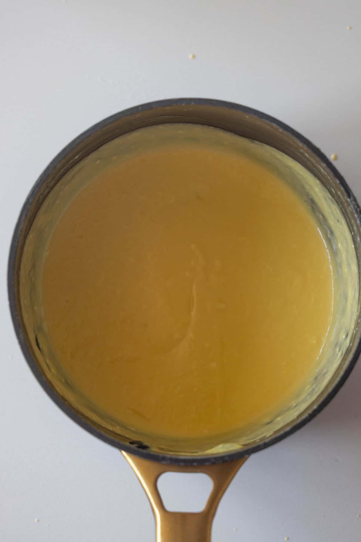 A saucepan filled with smooth, yellow Berries and Creme Anglaise sauce or custard, viewed from above on a light surface.
