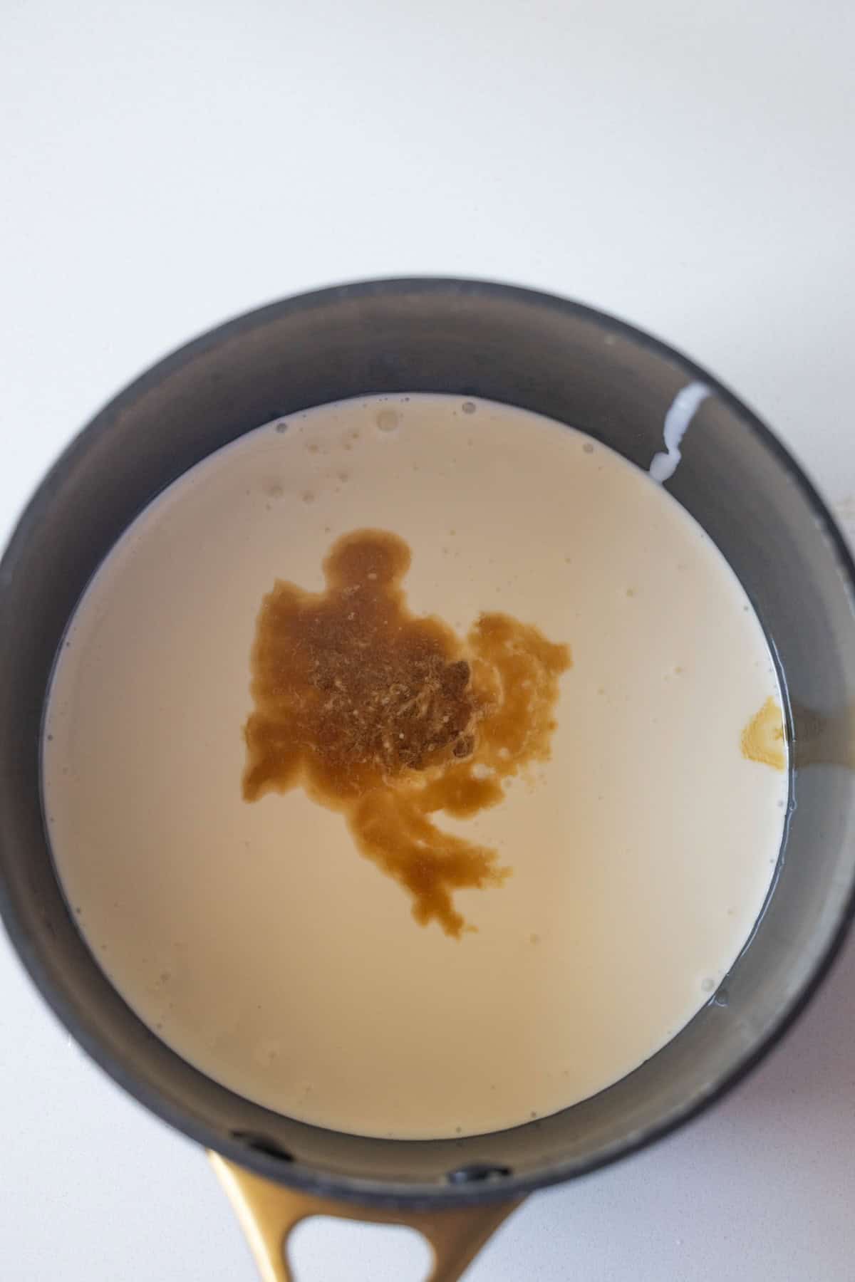 A saucepan containing milk with a brown liquid, likely vanilla extract, beginning to mix in—the first step in making Berries and Creme Anglaise.