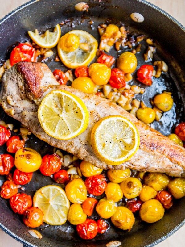 Grecian Pork Chops with meat, tomatoes, and lemons cooked in a frying pan.