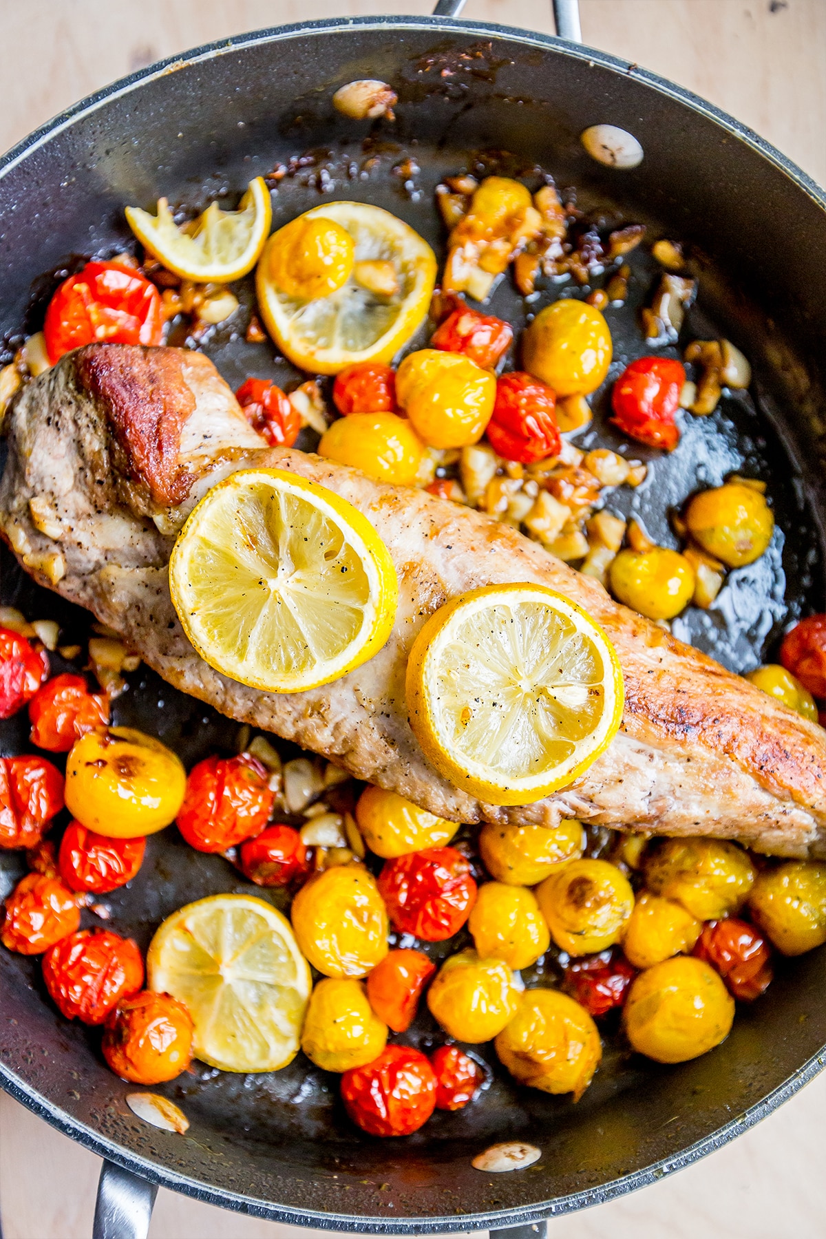 pan with pork tenderloin with lemons, garlic and tomatoes around it. 