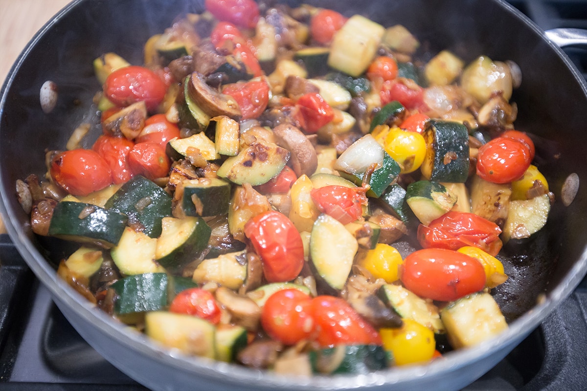 mushrooms, zucchini, onion, and tomatoes sauteed in a large pan. 