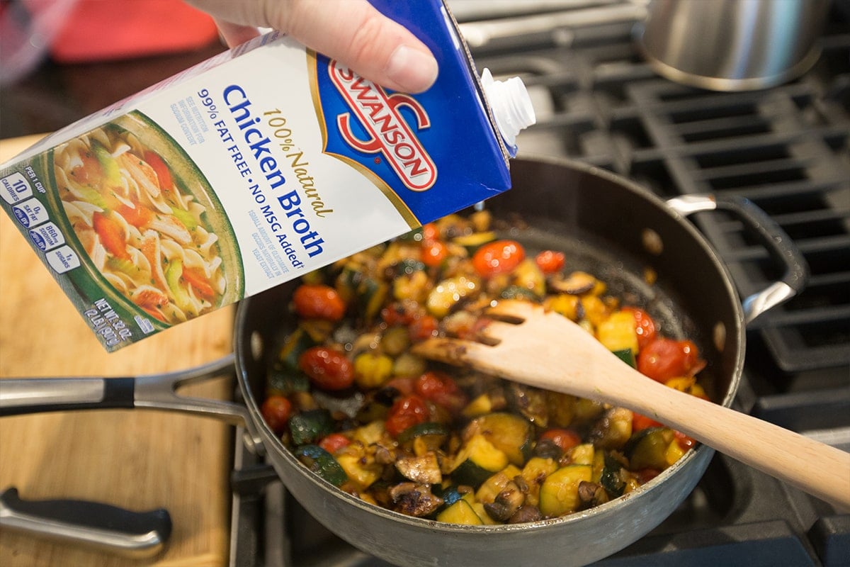 pan with sauteed vegetables in it, swanson chicken broth being poured over it. 