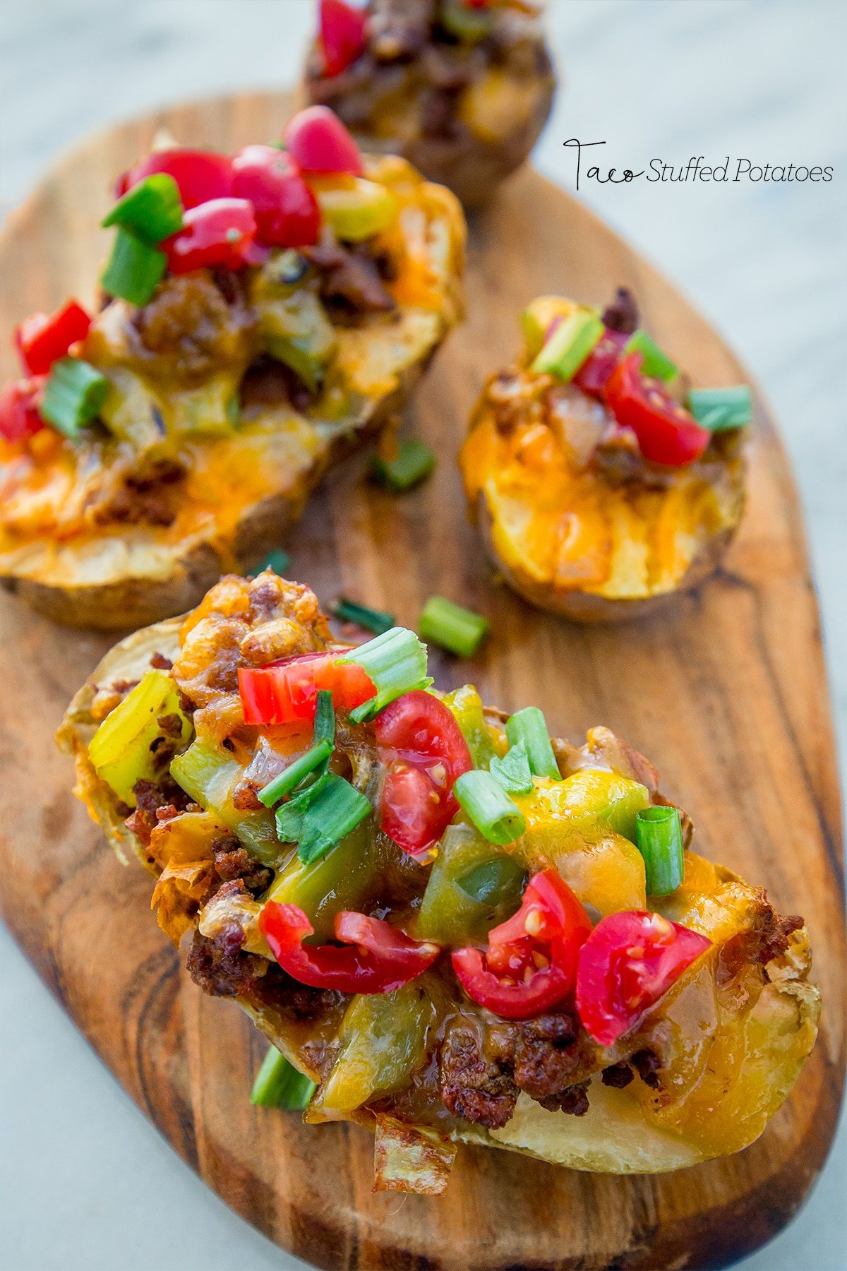 Potatoes hallowed out with taco filling in them and cheese melted on top with green onions on them. 