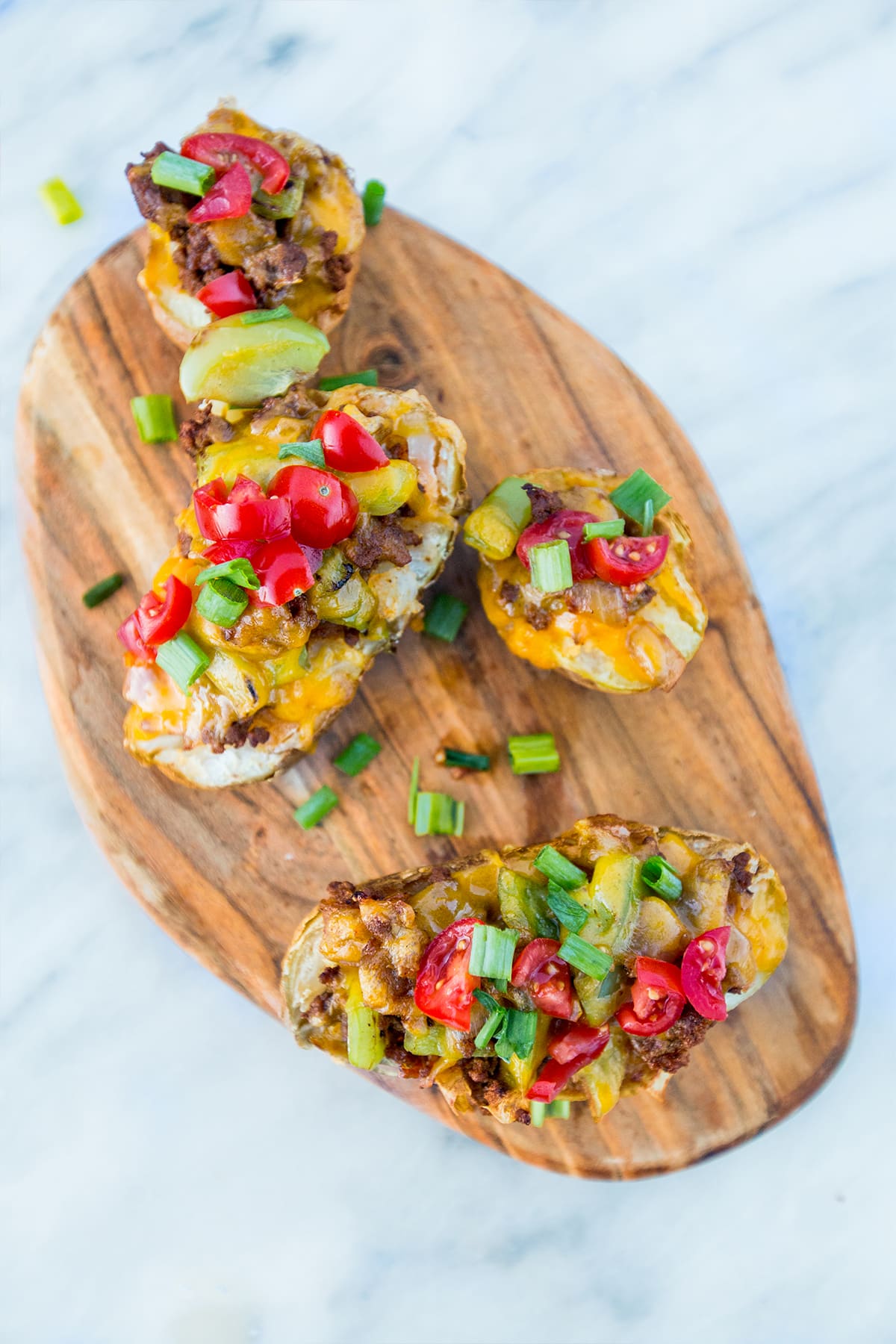 Potatoes hallowed out with taco filling in them and cheese melted on top with green onions and tomatoes on them. 