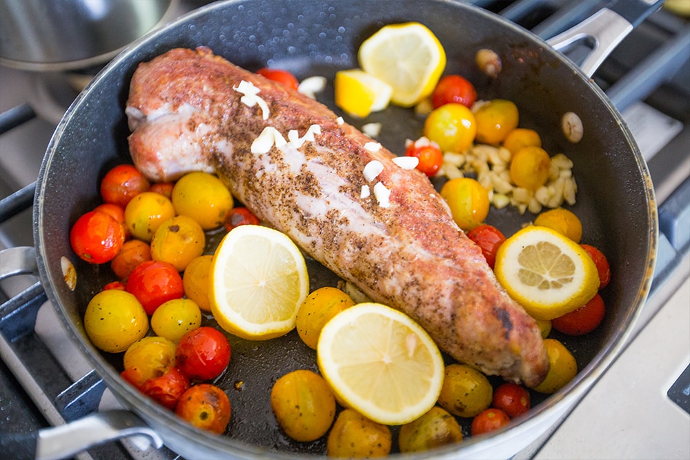 picture of pork tenderloin browning in pan with lemon, and tomatoes