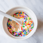 A bowl of cake batter ice cream with fudge sprinkles.