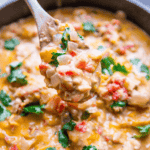 Close-up of a spoonful of creamy vegetable stew with diced tomatoes, onions, cilantro, and a rich, saucy base in a pot—a perfect companion to the delightful One Pot Cheesy Chicken and Green Chile Skillet.