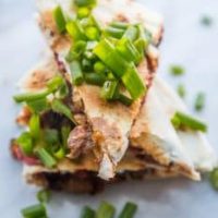 A stack of meaty vegan quesadillas topped with green onions.