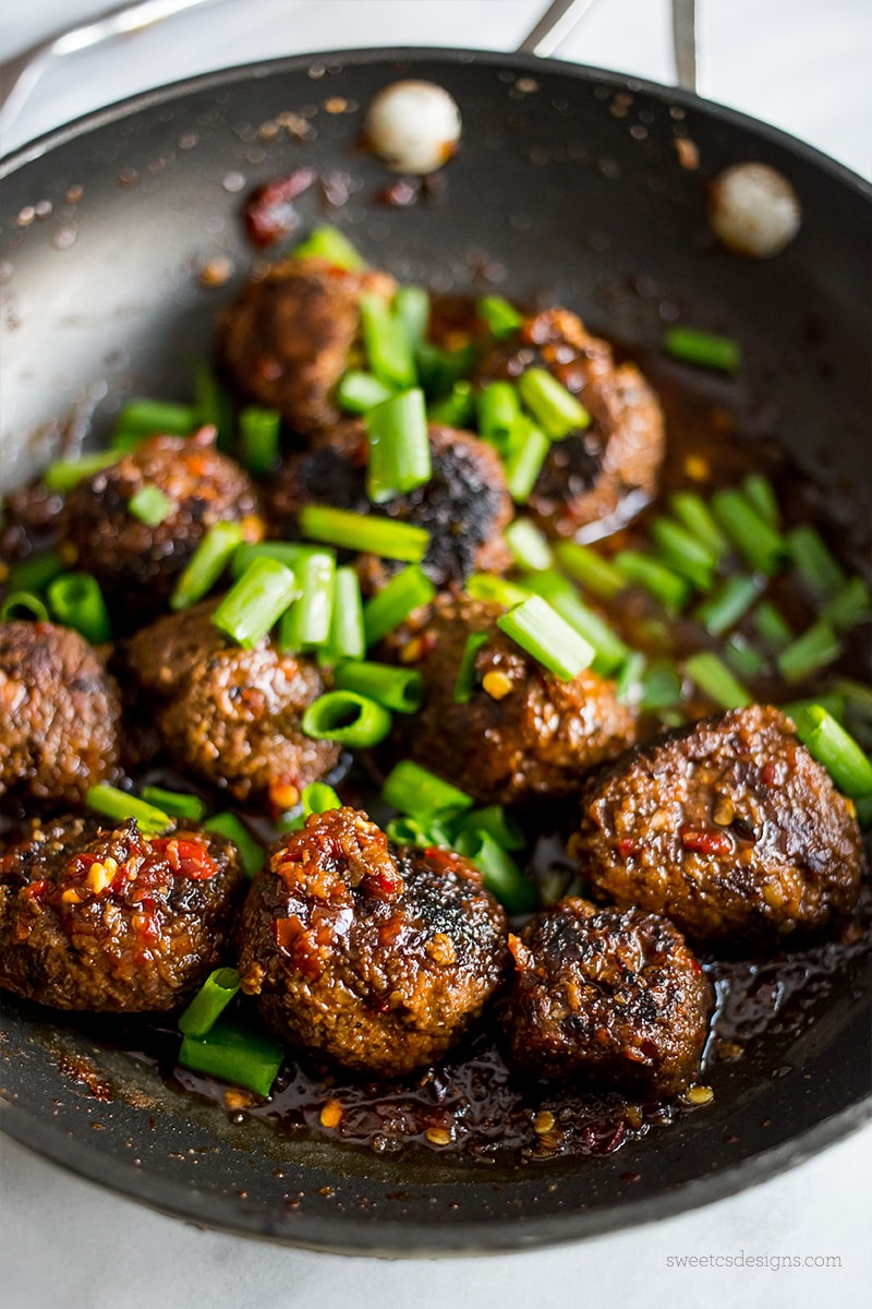 meatballs in a pile with rich Asian sauce on top and green onions