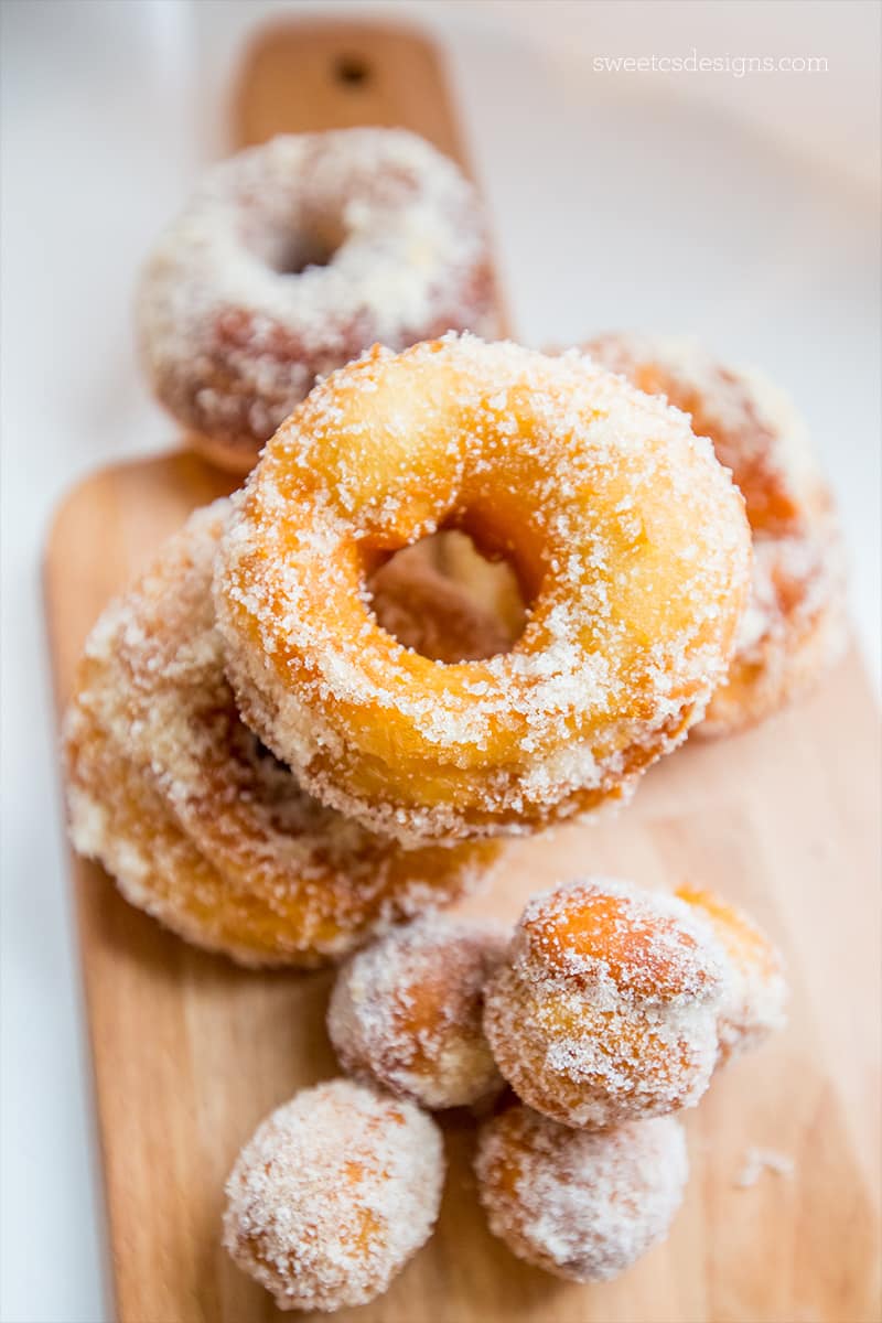 Donuts covered in powdered sugar on a wooden cutting board.