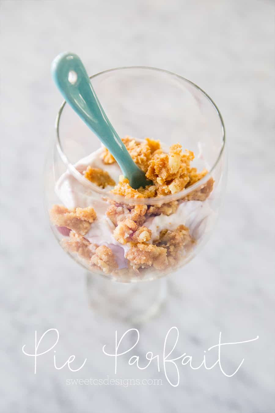 picture of leftovers in a wine glass with yogurt and granola clusters with blue spoon in it. 